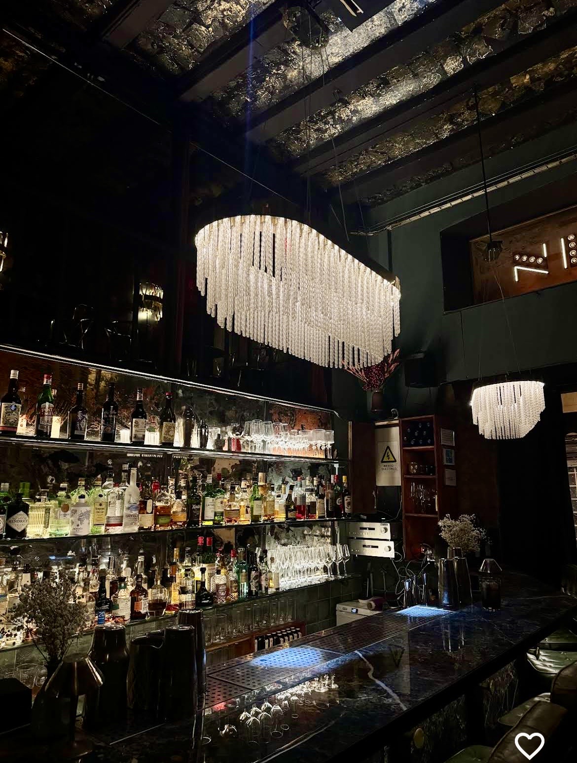 A cocktail bar with chandeliers and an illuminated display of bottles